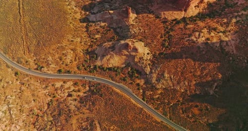 Two cars riding by the highway going through the desert landscape.