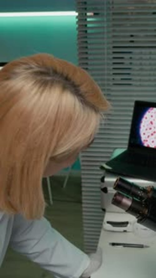 Woman Examining Sample Under Microscope in Lab