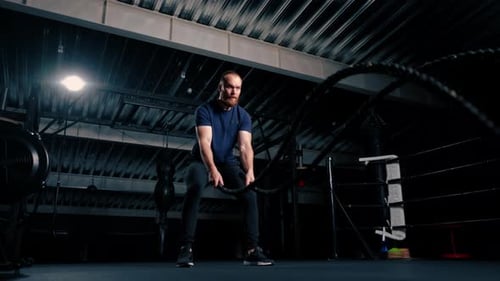 young male bodybuilder doing exercises with rope in hands in gym preparing for bodybuilding