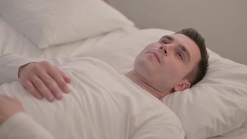 Réfléchissez à un jeune homme aux yeux ouverts allongé dans son lit