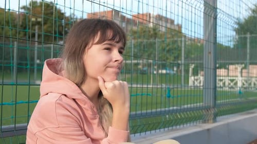 Thoughtful Woman Sitting by Urban Fence