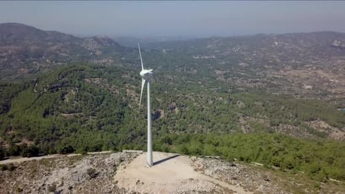 Aerial footage of Wind turbines spinning, in a mountain forest surrounding