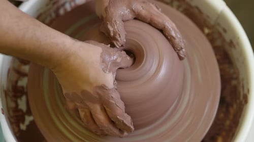 Close up skilled potter fingers forming wet clay shape spinning on workshop pottery wheel