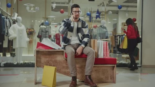 Man Relaxes at Mall Entrance Urban Scene Featuring Man with Bags Enjoying Holiday Atmosphere and