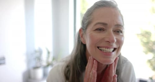 Senior Woman Smiling, Touching Her Neck in Bright Room