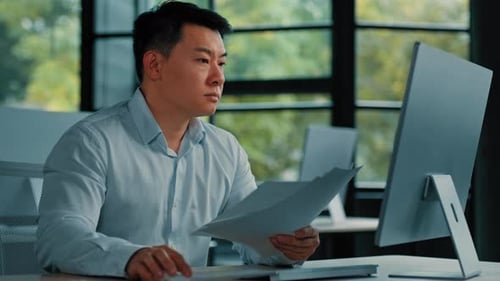 Tired Unhappy Asian Man Worker Manager Sit at Office Doing Routine Paperwork Read Contract Documents