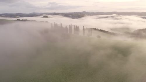 Aerial view of misty countryside with rolling hills and villa, Italy.