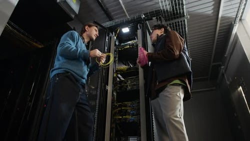 Two Network Engineers Holding Cable Coils and Talking in Data Center