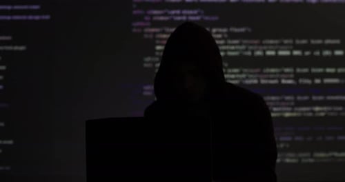 Unbekannter Hacker-Mann, der ein Sweatshirt mit Kapuze trägt und auf der Tastatur den Programmiercode auf einem