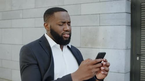 Upset african american businessman receives bad news on mobile phone in modern city