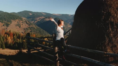 Young Woman Enjoying Freedom in Mountain Landscape Sitting on Wooden Fence with Open Arms