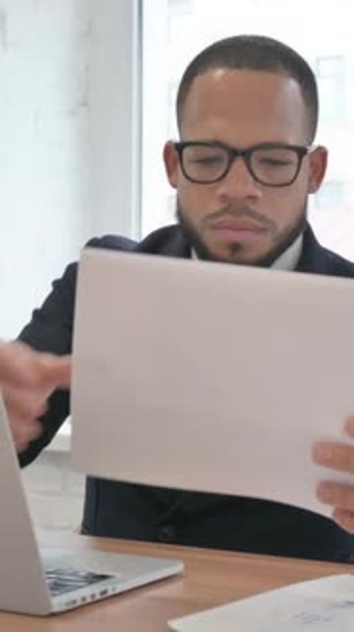 Man Reviews Documents at Desk with Laptop