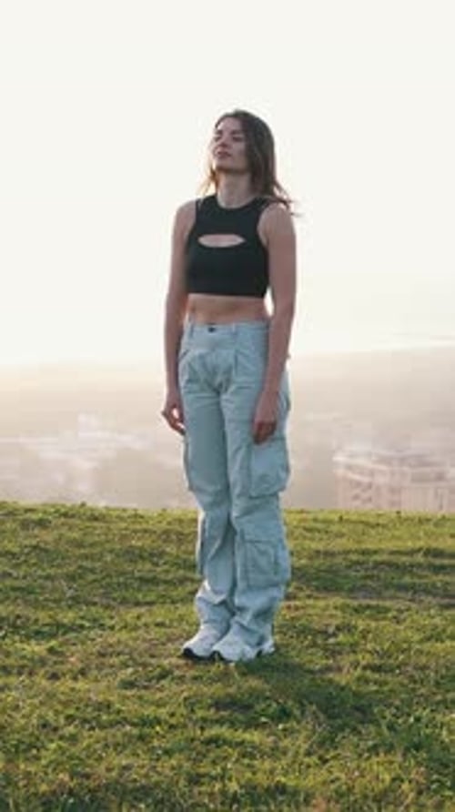Stylish young woman dancing on hilltop with city view
