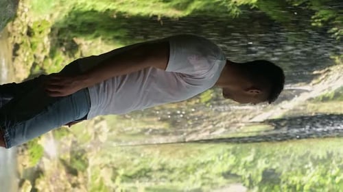 Man sitting, marveling at waterfall's beauty in lush park. Perfect for eco-tourism, nature excursion
