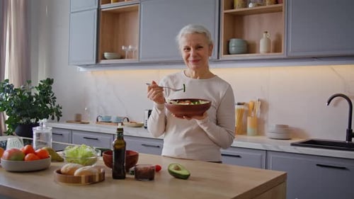 Senior Woman Enjoys Eating Fresh Salad in Kitchen