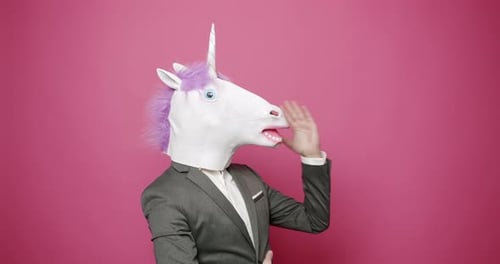 Geschäftsmann mit Einhornmaske gestikuliert im rosa Studio
