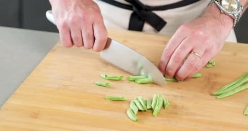 männlicher Koch schneidet seine grüne Bohne mit seinem Messer auf dem Schneidebrett in seiner Küche in große Stücke