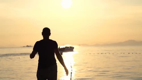 Silhouette of a man walking on a golden beach at sunset in super slow motion