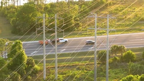 Linhas de energia em altos postes de aço se estendem por rodovias com carros de condução rápida e transmissão de eletricidade