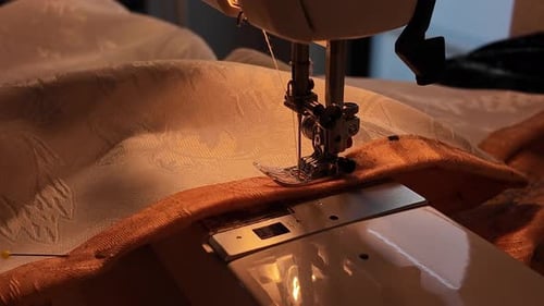 Close up of person sewing fabric on a sewing focusing on the needle and hand guiding the material.