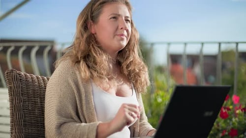 Freelancerin arbeitet an einem Laptop, während sie draußen auf einem gemütlichen Stuhl sitzt