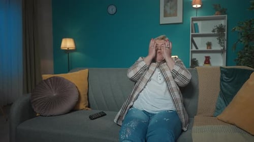 In the Picture an Elderly Woman is Sitting on a Sofa in an Apartment She Looks Away As If Watching a