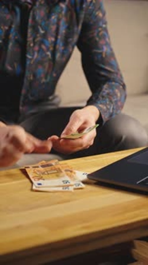 Man Counting Euros on Table with Laptop
