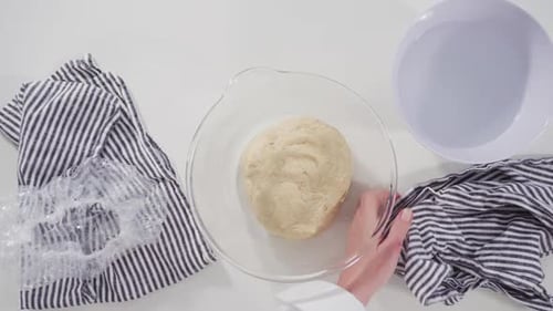 Hands Kneading Dough in Glass Bowl on Table