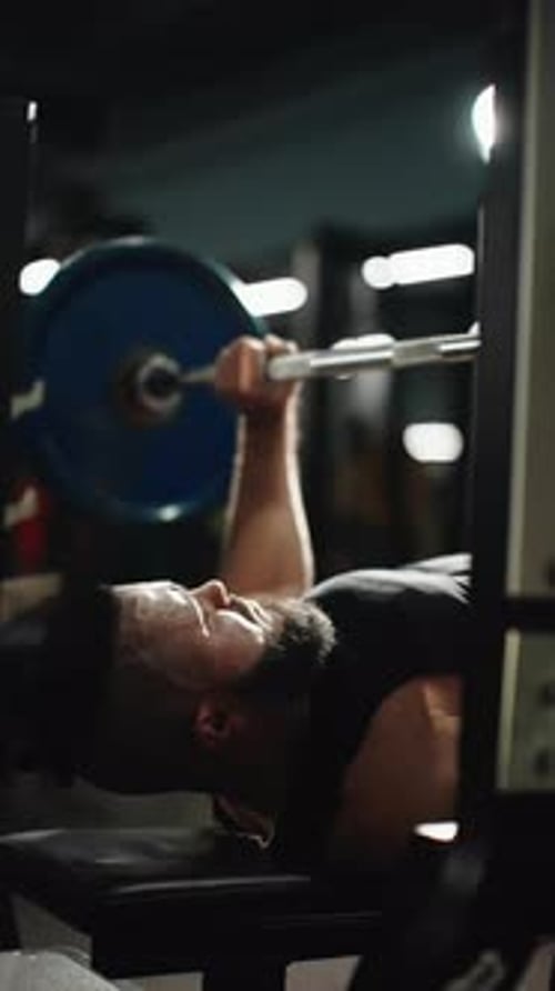 Muscular Athlete Performing Heavy Bench Press Straining Muscles Against Barbell in Dark Gym