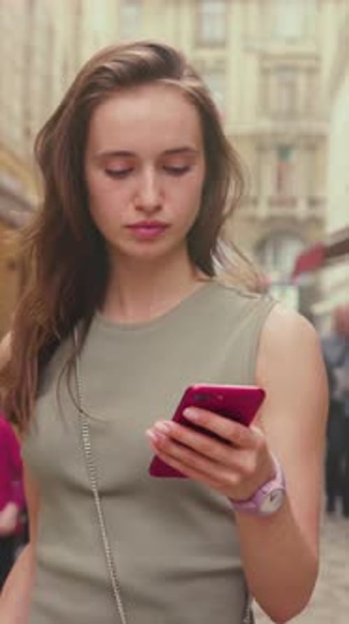 Reflective Young Lady Using Phone Amidst City Crowd City Wanderer Consults Map on Pink Device During