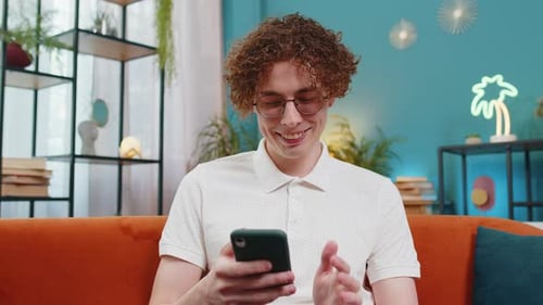 Smiling Man Using Smartphone on Orange Couch Indoors