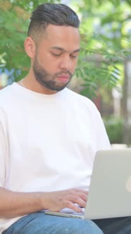 Young man works on laptop outdoors during the day