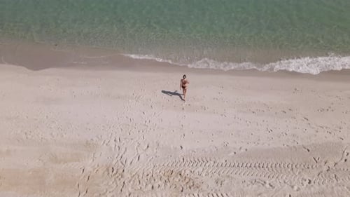 Young Caucasian woman in bikini walks on sandy beach toward warm water