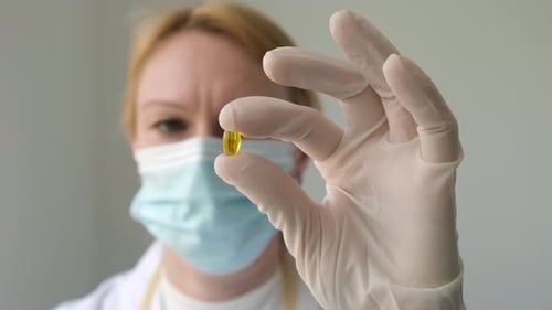 Close Up Hand of Female Doctor in Gloves Holding Yellow Omega 3 Capsule