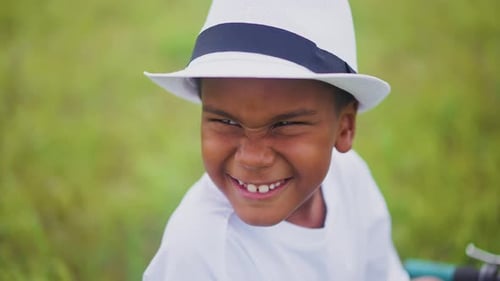 Cheerful Child Wearing a White Hat Smiles Brightly in a Green Field