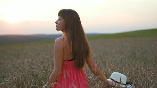 Young Pretty Woman in Red Summer Dress Standing on Yellow Farm Field with Ripe Golden Wheat Enjoying