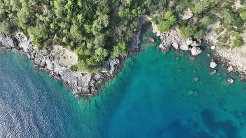 Aerial top view of a coastal cliffside with vivid turquoise sea.