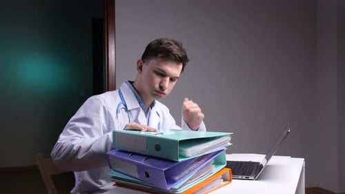 Tired Doctor With Documents Sitting at Desk