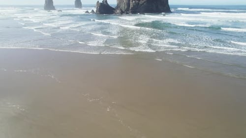 Ocean waves rush past Haystack Rock and crash onto the beach