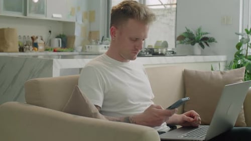 Man Using Phone and Laptop at Home