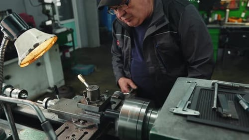 Cinematic shot of an elderly turner processes the metal part on a lathe in a lathe shop