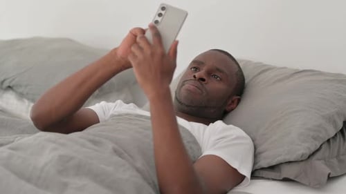 Young Adult Using Cell Phone Relaxing in Bed
