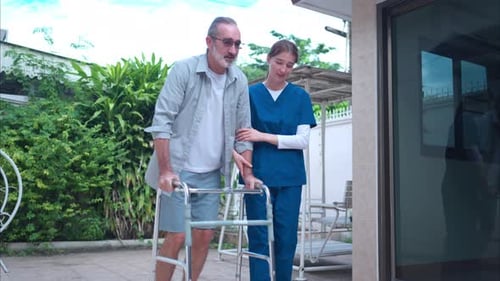 Elderly man holding a walking aid while being assisted by a young female caregiver learning to walk