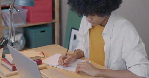 Teen Student Writing in Notebook at Desk