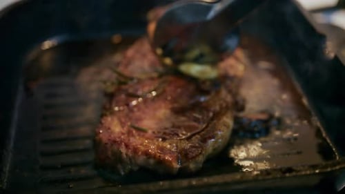 Close up of a juicy steak sizzling in a grill pan while being pressed with a spatula