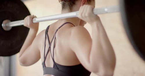 Focused unaltered caucasian woman free weight training at gym lifting barbell, in slow motion