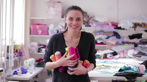 Cute Caucasian Seamstress or Dressmaker Keeps Colorful Spools of Thread in Hands on Atelier Shop