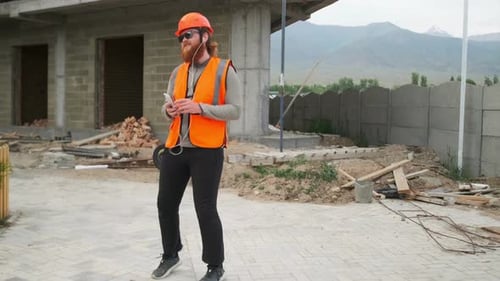 Trabalhador da construção civil dançando de bom humor ouve música em fones de ouvido, canteiro de obras