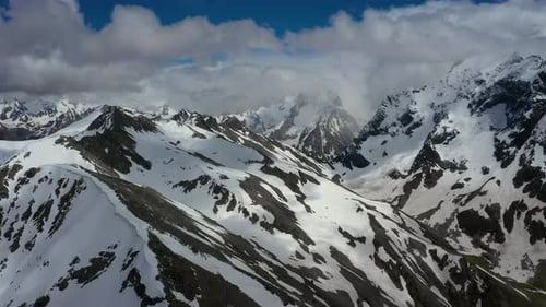 Air flight through mountain clouds over beautiful snow-capped peaks of mountains and glaciers.