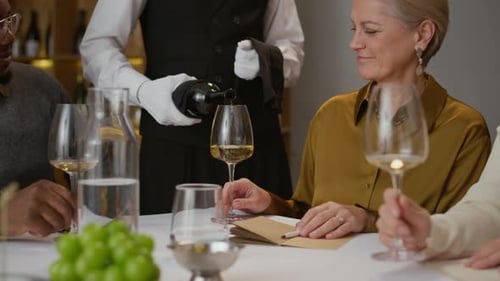 Sommelier Serving White Wine to Diverse Customers in Restaurant
